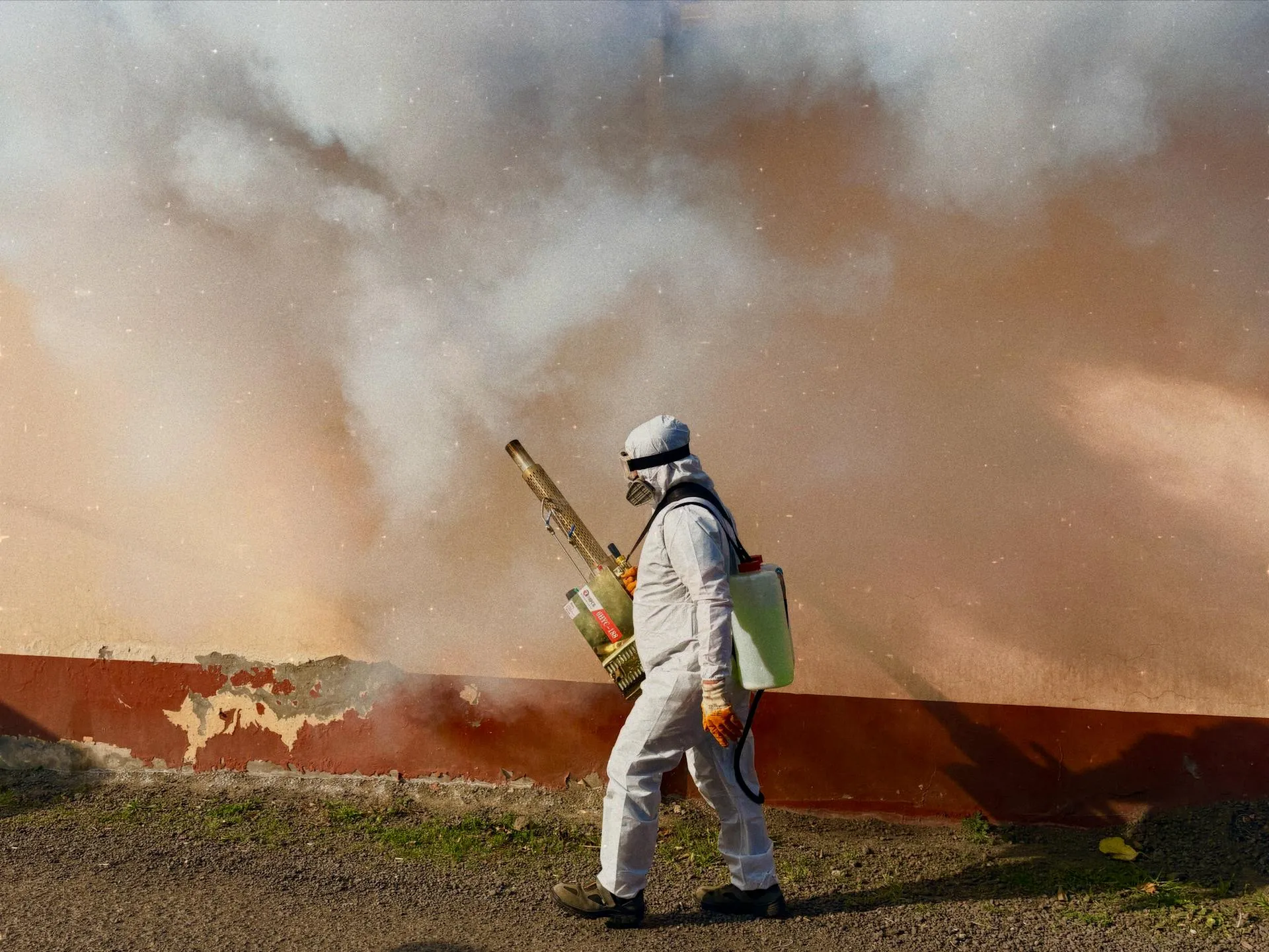 Pest control worker in full protective coverall and respirator completing an outdoor treatment with backpack sprayer
